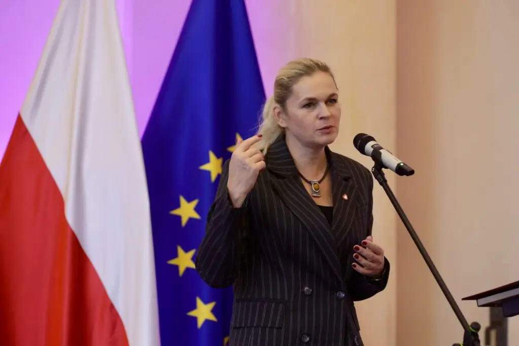 A speaker addressing the fourth Summit for Education in front of Polish and EU flags
